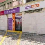 Stokarea - Mini Armazens Self storage Vista externa da entrada de uma unidade de autoarmazenamento STOKAREA, com uma fachada roxa e laranja com detalhes de contato e ícones de serviço na porta, em frente a uma passarela de paralelepípedos. Lidar em Portugal