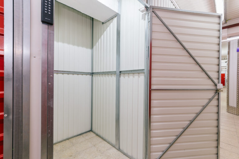 Stokarea - Mini Armazens Self storage A unidade de Self Storage Stokarea oferece uma vista de um pequeno espaço de armazenamento vazio com paredes de metal corrugado branco e uma porta de correr aberta. O piso de ladrilho e a iluminação fluorescente realçam sua aparência limpa e organizada, ideal para quem busca mini armazéns para alugar. Lidar em Portugal