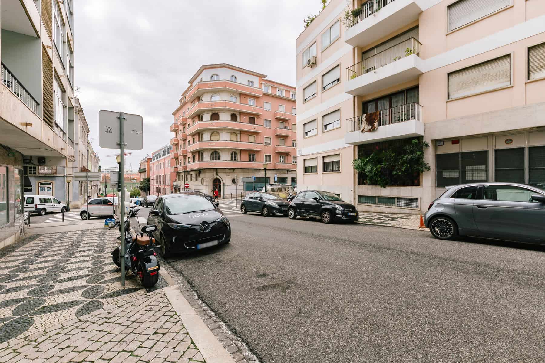 Stokarea - Mini Armazens Self storage Vista da rua de uma área urbana europeia com prédios de vários andares, alguns com varandas. Carros alinham a rua, e uma scooter está estacionada perto da calçada estampada. O céu nublado sugere um dia nublado, enquanto o Stokarea Self Storage nas proximidades oferece mini armazéns para alugar para sua conveniência. Lidar em Portugal