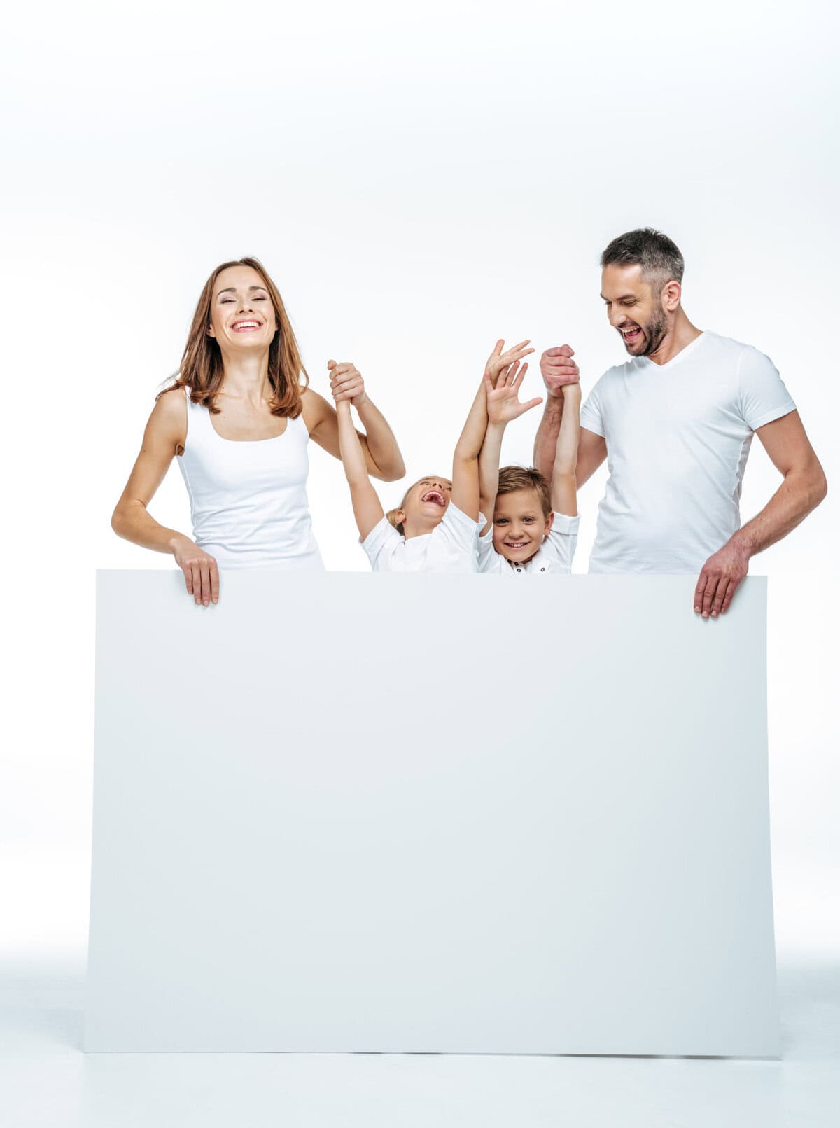 Stokarea - Mini Armazens Self storage Uma família alegre de quatro pessoas, vestindo roupas brancas, está de pé com as mãos levantadas atrás de um grande quadro branco em branco. Os pais, um homem e uma mulher, seguram as mãos dos filhos, que estão sorrindo e espiando por cima do quadro. Lidar em Portugal