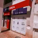 Stokarea - Mini Armazens Self storage Vitrine com uma placa vermelha e branca onde se lê STOKAREA, número de contato e site. A janela exibe ícones de serviços como armazenamento de documentos, armazenamento de móveis, estacionamento de veículos, caixas e entrega. Lidar em Portugal